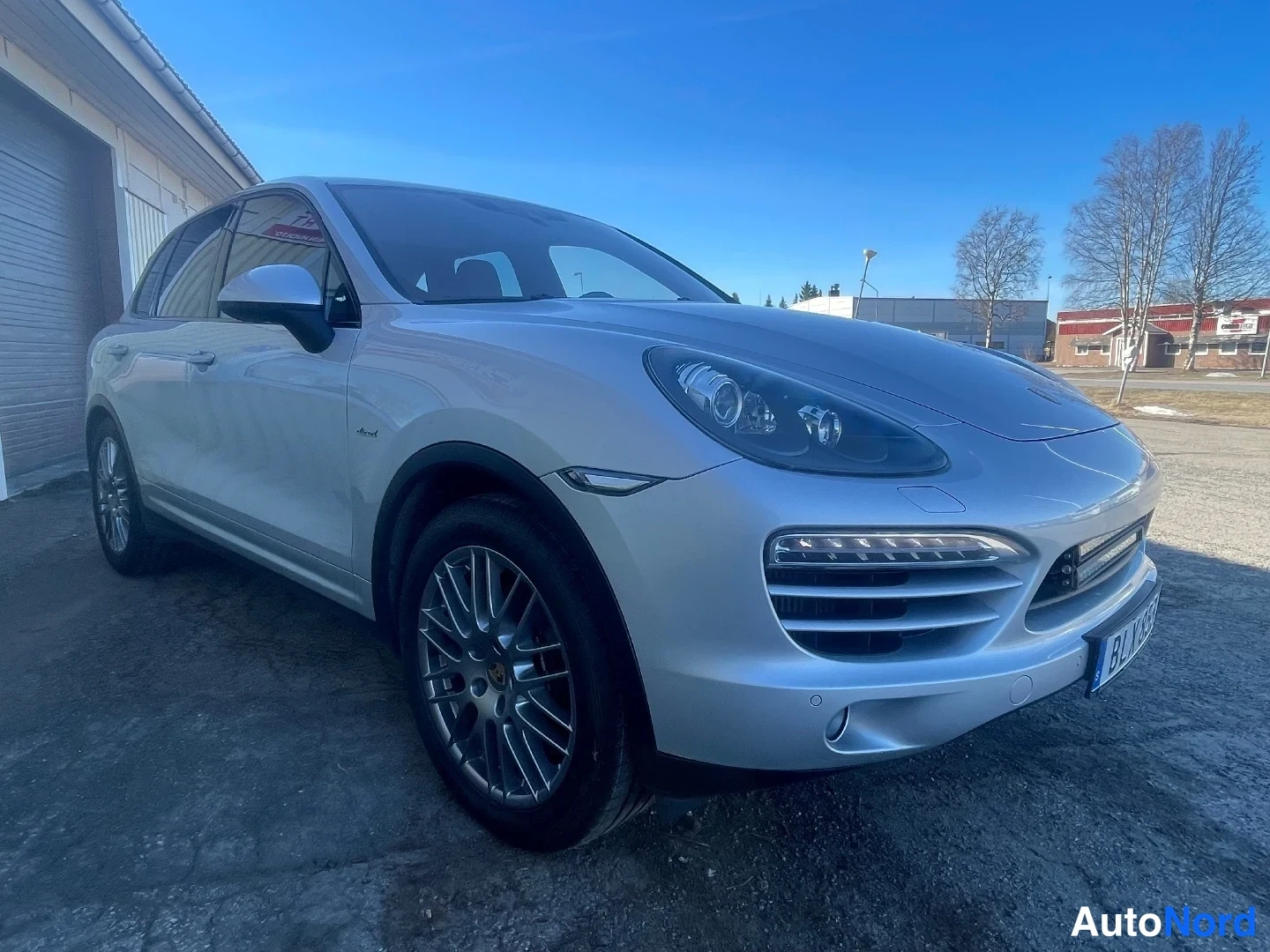 Etuviisto, nokka oikealle: Hopeainen Porsche Cayenne etuviistöstä oikealta, etupuskurin ja kyljen näkyvät.