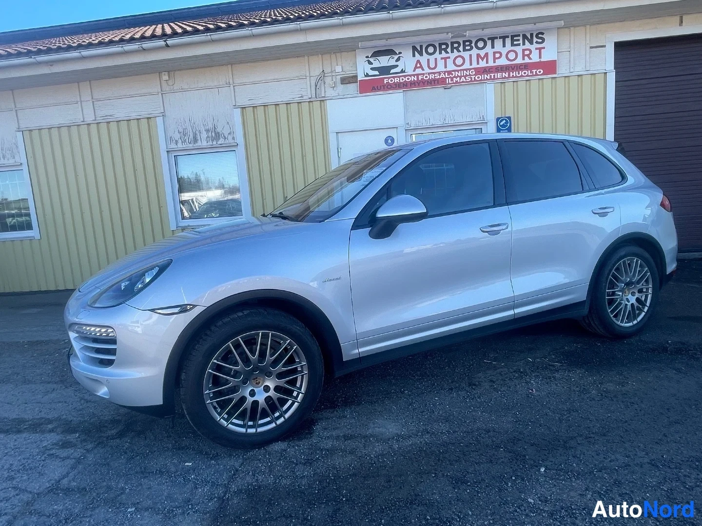 Etuviisto, nokka vasemmalle: Hopeainen Porsche Cayenne etuviistöstä vasemmalta talon edessä.