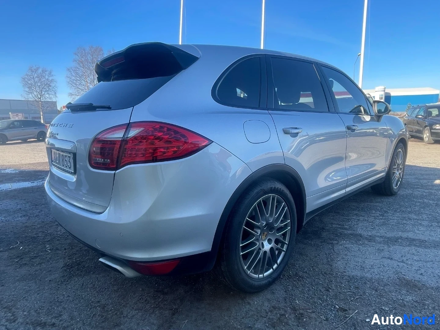 Takaviisto: Hopeanharmaa Porsche Cayenne takaa vasemmalta kuvattuna auringossa, rekisterikilpi ja kevytmetallivanteet näkyvissä.
