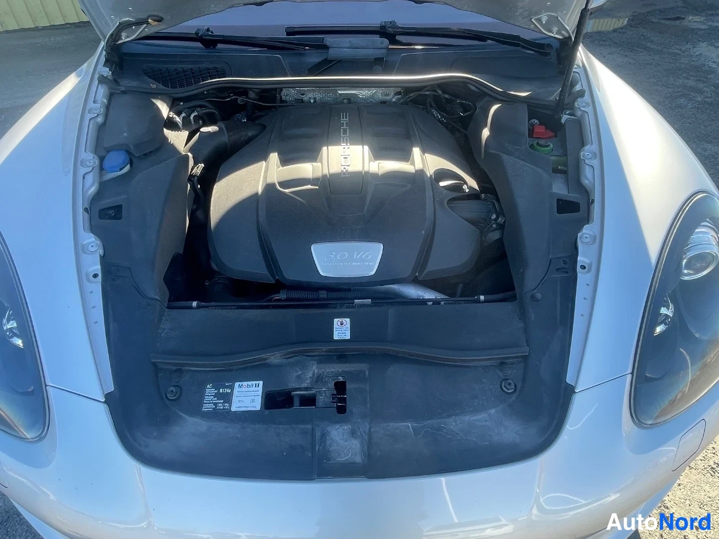 Edestä: Avattu moottoritila, Porsche-merkitty moottorin suojakansi tekstillä 30 V6, valoisa kuva.