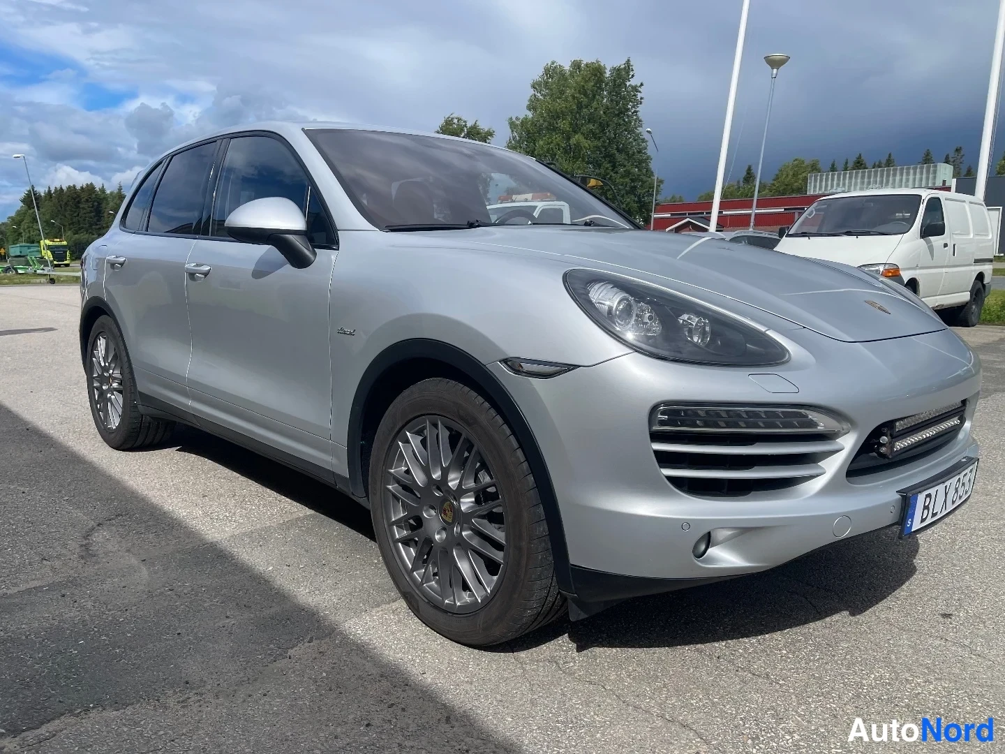 Etuviisto, nokka oikealle: Porsche Cayenne -maasturin keula ja vasen kylki kolmeneljäsosan etukuvassa; hopeakorinen auto suunnattuna kuvan oikealle, ajoneuvoa vastapäätä valkoinen