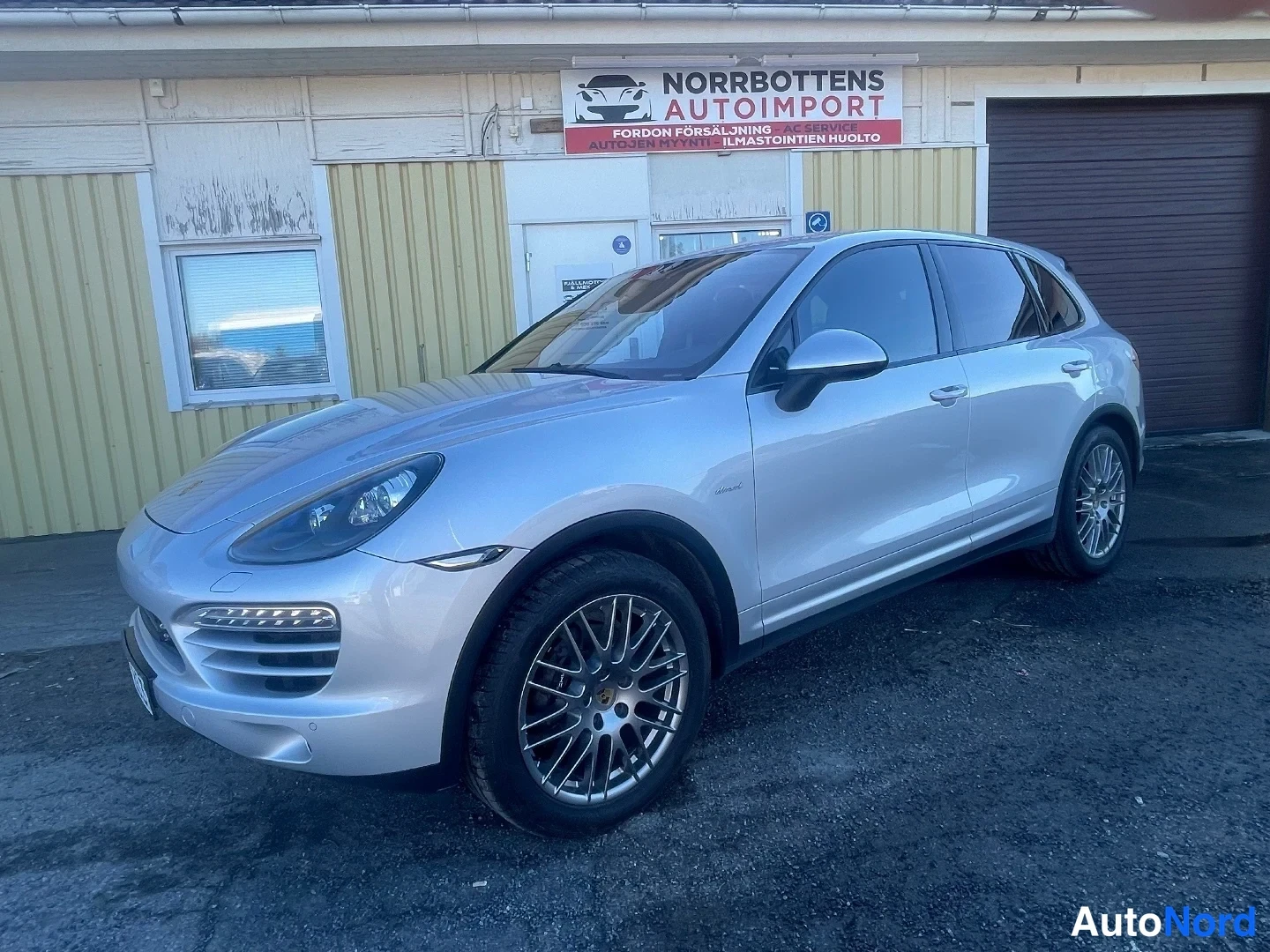 Etuviisto, nokka vasemmalle: Porsche Cayenne -maasturin keula ja vasen kylki kolmeneljäsosan etukuvassa auton ollessa käännettynä kuvan vasemmalle; hopeakorinen auto Norrbottens Au