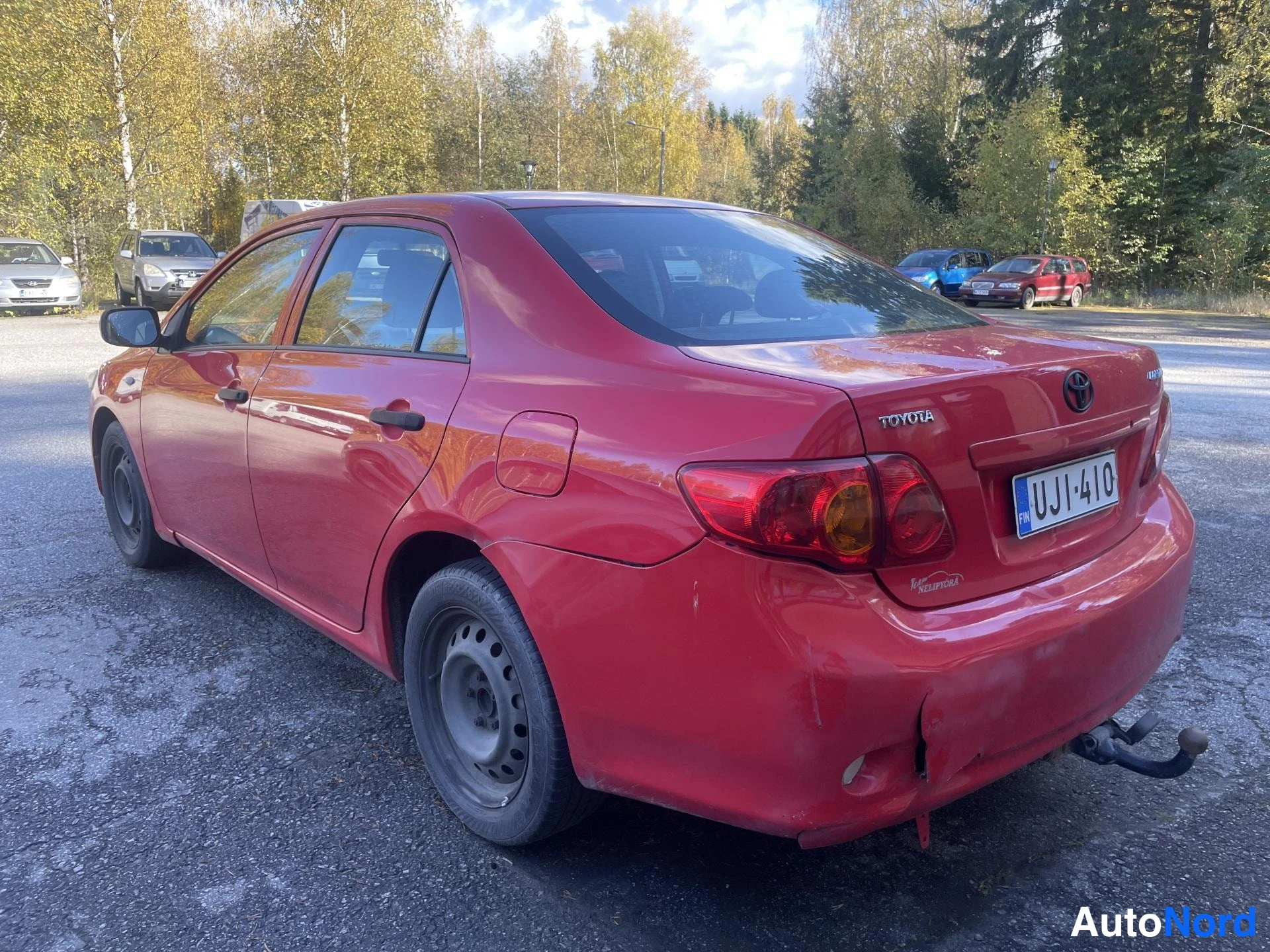 Takaviisto: Punaisen sedanin takaosa ja vasen sivu kuvattuna parkkipaikalla, rekisterikilpi ja takaluukissa TOYOTA-teksti.