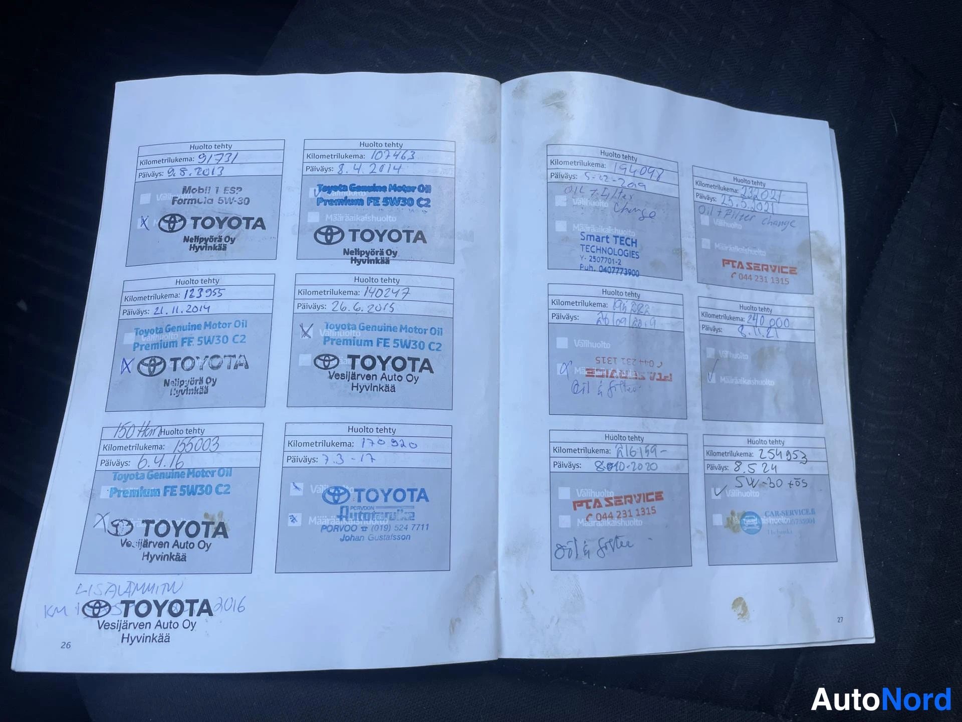 Yksityiskohta: Auki avattu huoltokirja sivuilla käsinkirjoitettuja huoltomerkintöjä ja Toyota-huoltoleimoja.