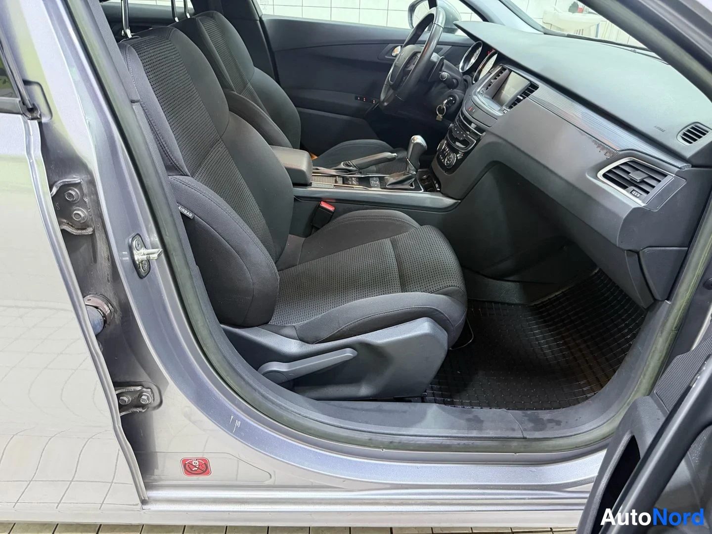 Muu: Peugeot-henkilöauton etuistuin ja tumma keskikonsoli näkyvät avatun etuoven kautta.