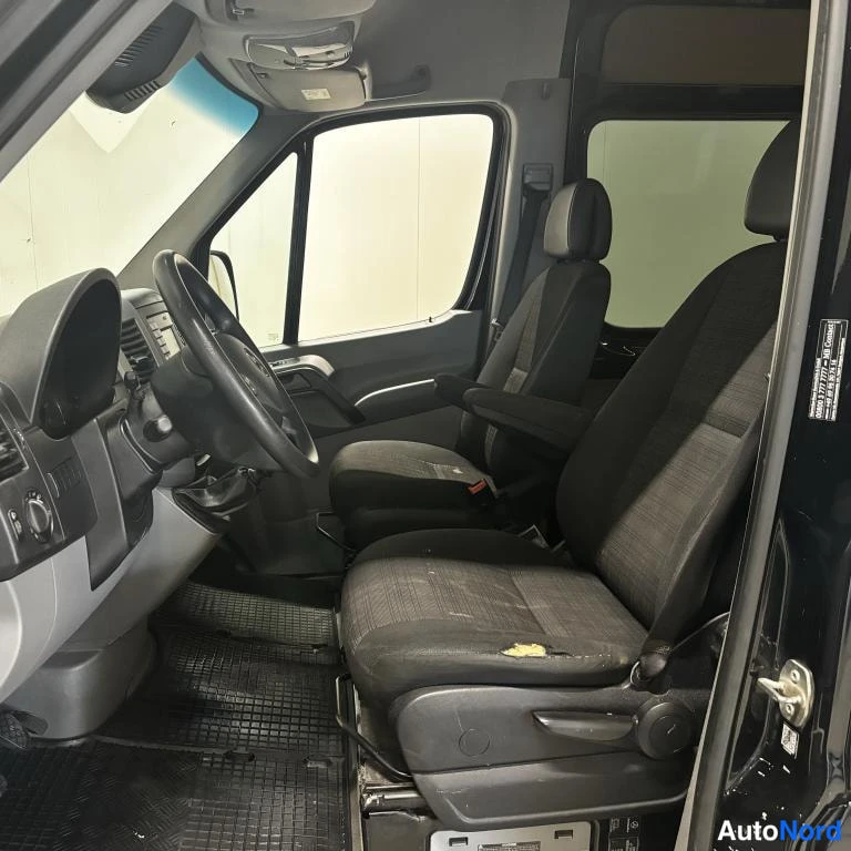 Muu: Mercedes-Benz Sprinter -pakettiauton ohjaamo; ohjauspyörä, kaksi mustaa kangasistuinta ja tummat matot.