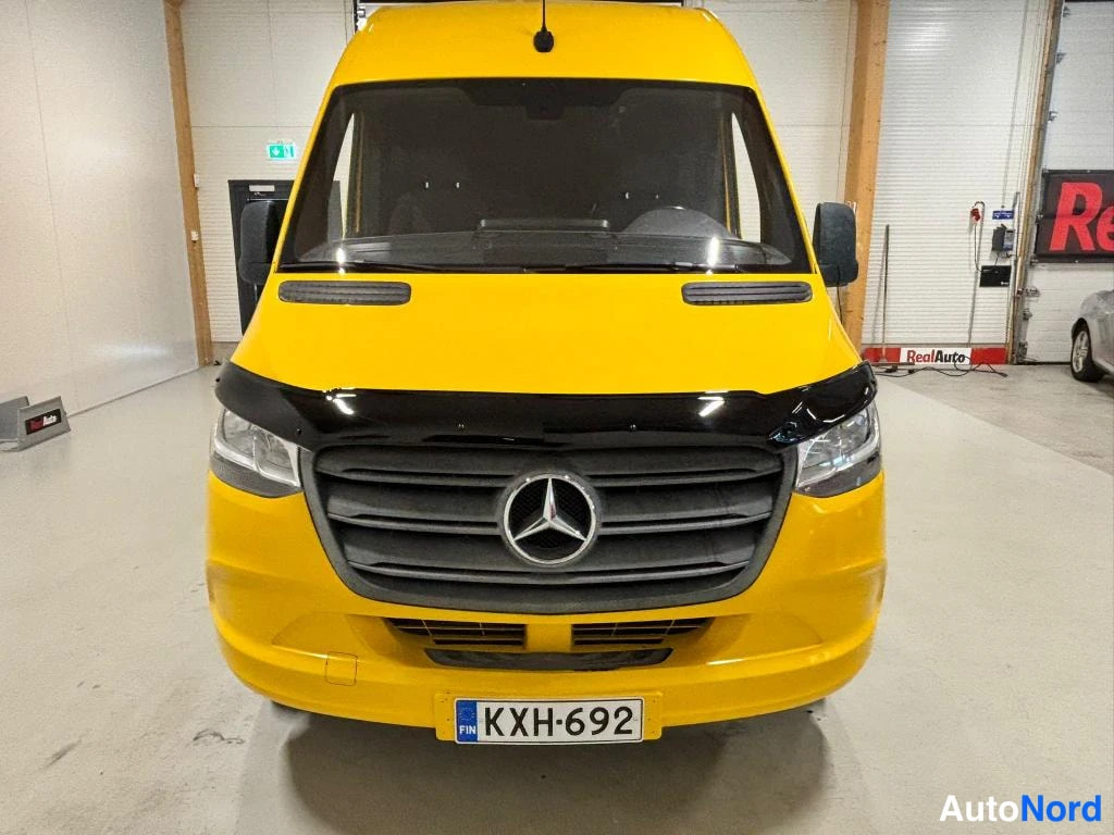 Edestä: Keltainen Mercedes-Benz Sprinter suoraan edestä, musta etusuoja ja rekisterikilpi.