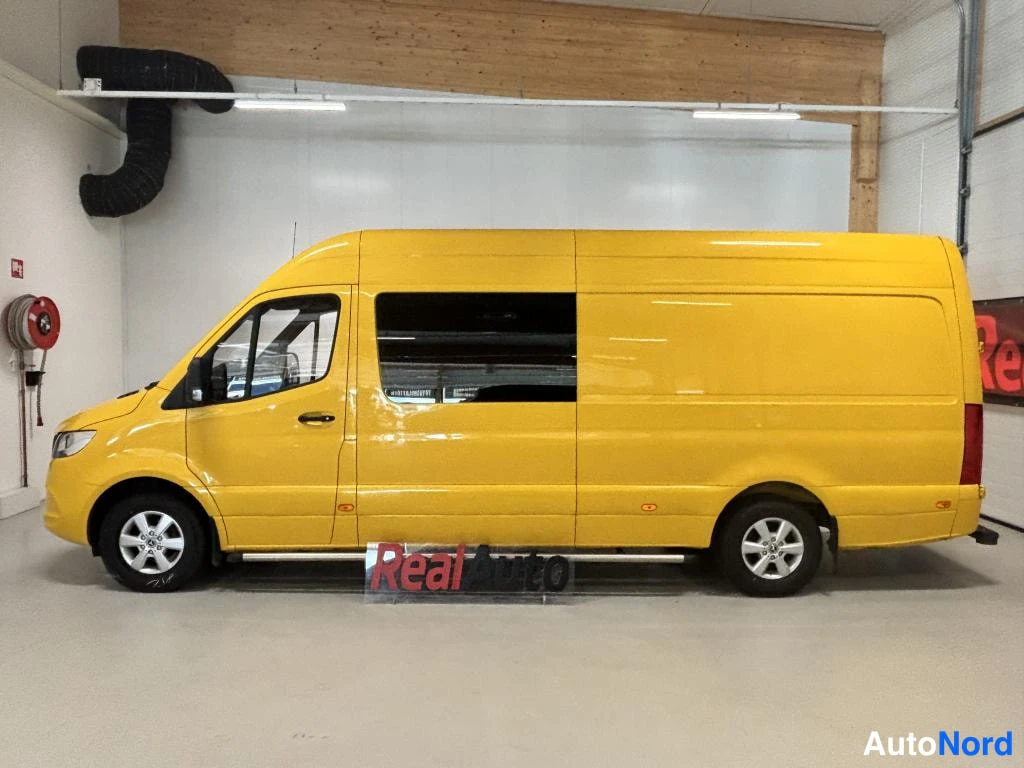Sivulta: Keltainen Mercedes-Benz Sprinter -pakettiauto kokonaan kyljestä sisätiloissa, avattava takaovi ja myös takaosa vasemmalla.