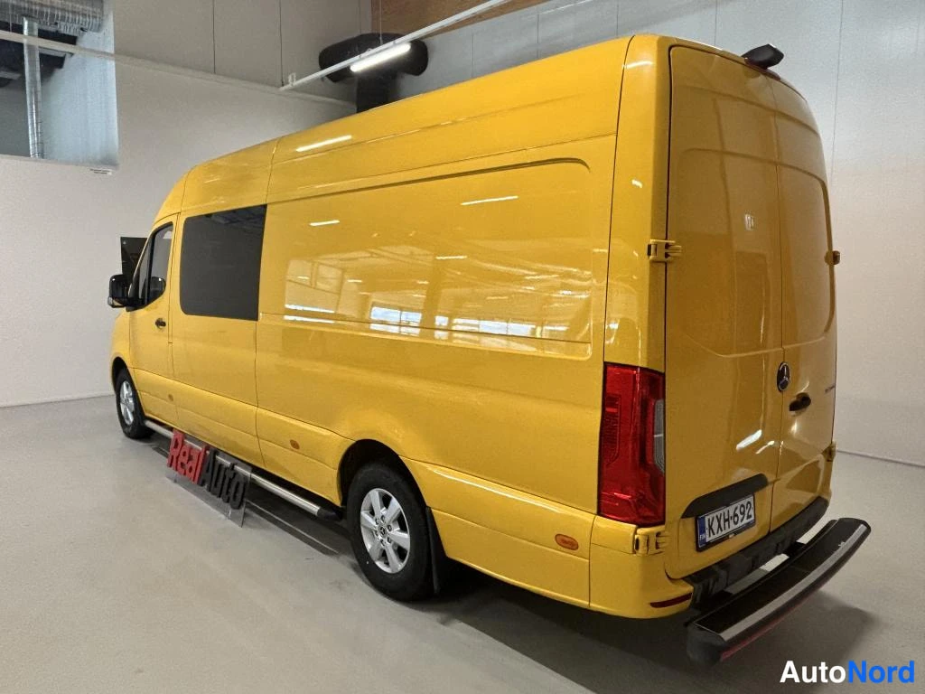 Takaviisto: Keltainen Mercedes-Benz -pakettiauto takaa viistosta kuvattuna sisätiloissa; rekisterikilpi ja vasen kylki näkyvissä.