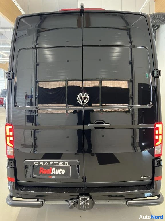 Takaa: Ajon takaa tunnistettava tummansininen tai musta Volkswagen Crafter -pakettiauto; takaluukussa CRAFTER-teksti ja RealAuto-kilpi.