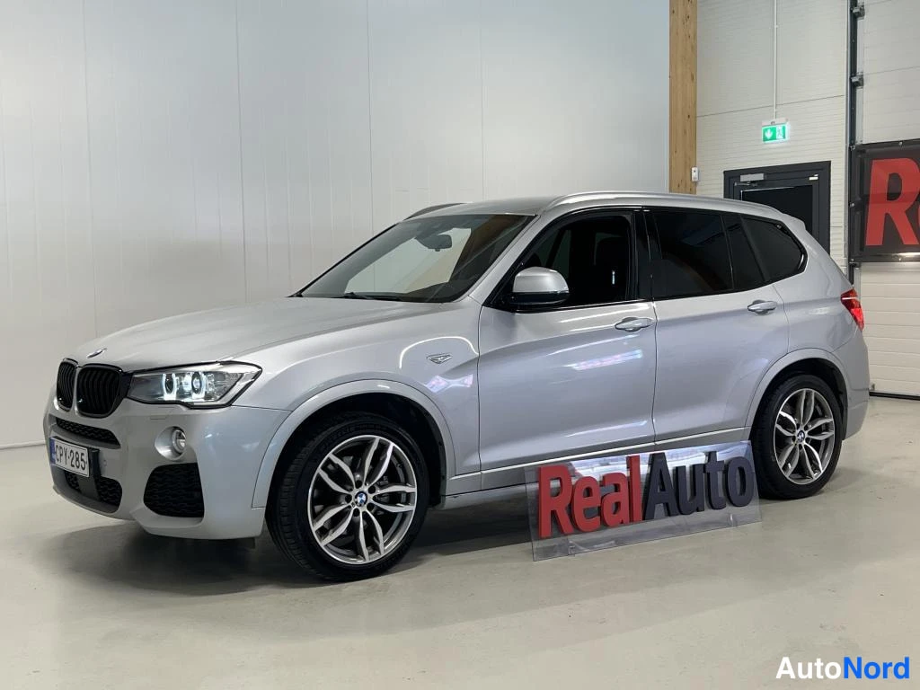 Etuviisto, nokka vasemmalle: BMW X3 -maastauto hopeana, etukulma, RealAuto-tunnuksella ja rekisterikilvellä.