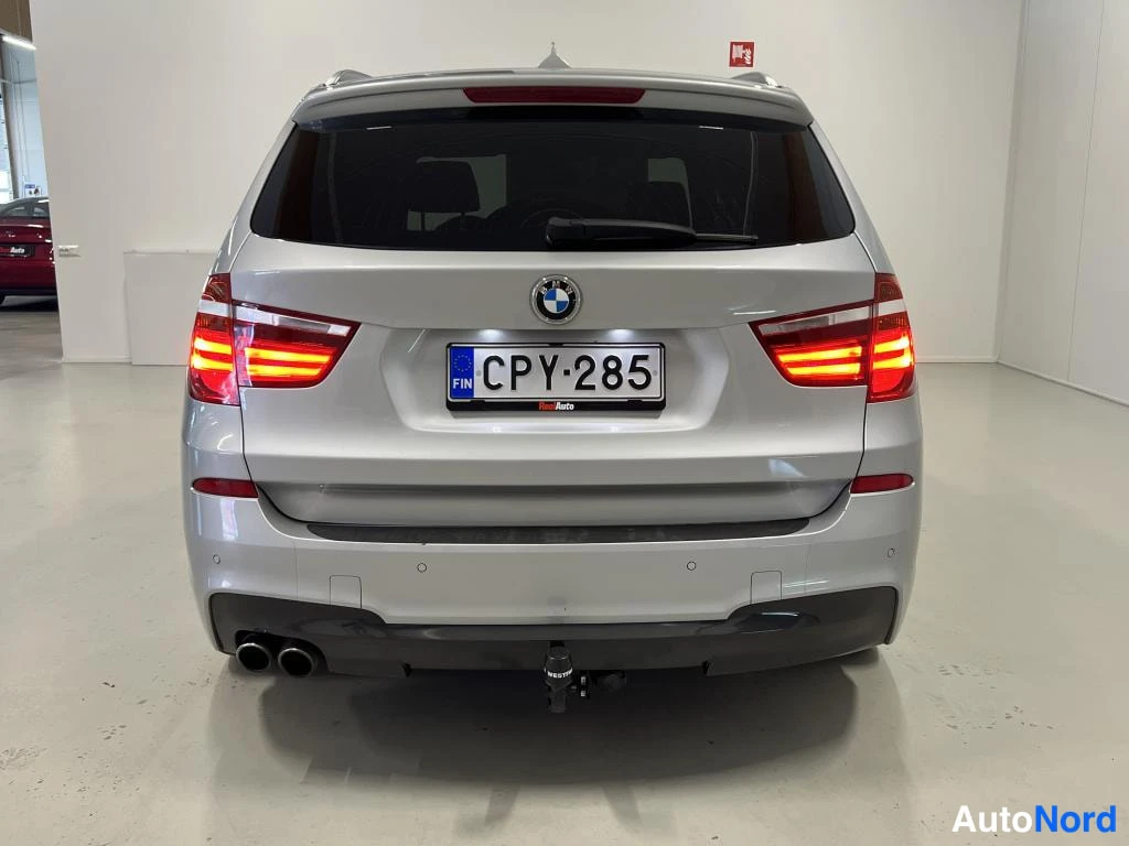 Takaa: Hopeanvärinen BMW X3 suoraan takaa kuvattuna, rekisteritunnus, takavalojen kirkkaat LED-paisteet, takapuskurissa vetokoukku ja kaksoispakoputket sisätilassa.