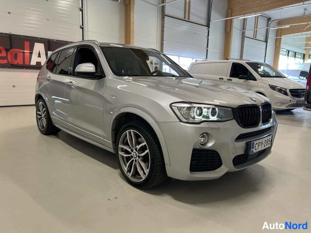 Etuviisto, nokka oikealle: Hopeanvärinen BMW X3 etukulmasta kuvattuna autotallissa, rekisteritunnus, etuvilkut LED-paneeleilla, musta etugrilli ja keulan spoileri, taustalla valkoi