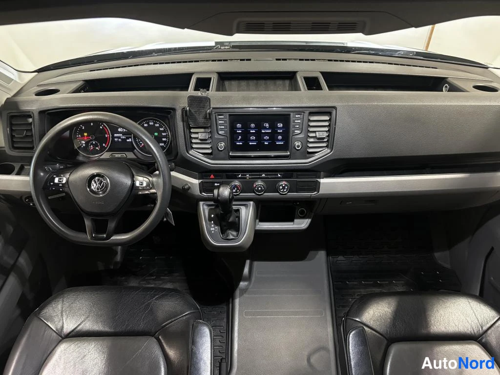 Muu: Auton sisätilat etuovista kuvattuna: Volkswagen-ohjauspyörä, mittaristo, kosketusnäyttö-autoradio, automaattivaihteen valitsin ja kaksi nahkaista etuistuinta.