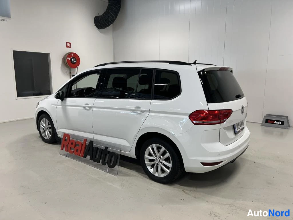 Takaviisto: Valkoinen Volkswagen Touran takaviistosta sisätiloissa.