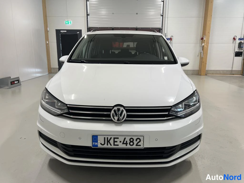Edestä: Valkoinen auto suoraan edestä kuvattuna, etusäleikössä VW-merkki ja -rekisterikilpi näkyvät.