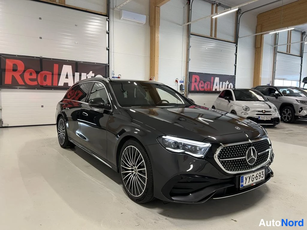 Etuviisto, nokka oikealle: Musta Mercedes-Benz farmaria etuosa kolmivärtistesti oikealta, keulavalo ja lattamattori näkyvät.