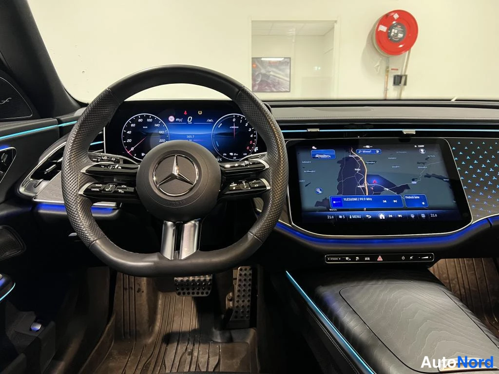 Muu: Mercedes-Benzin ohjaamo: nahkainen ohjauspyörä, digitaalinen mittaristo ja keskitörmäisen infotainment-näyttö, jolla on kartta; sininen ympäristövalaistus.