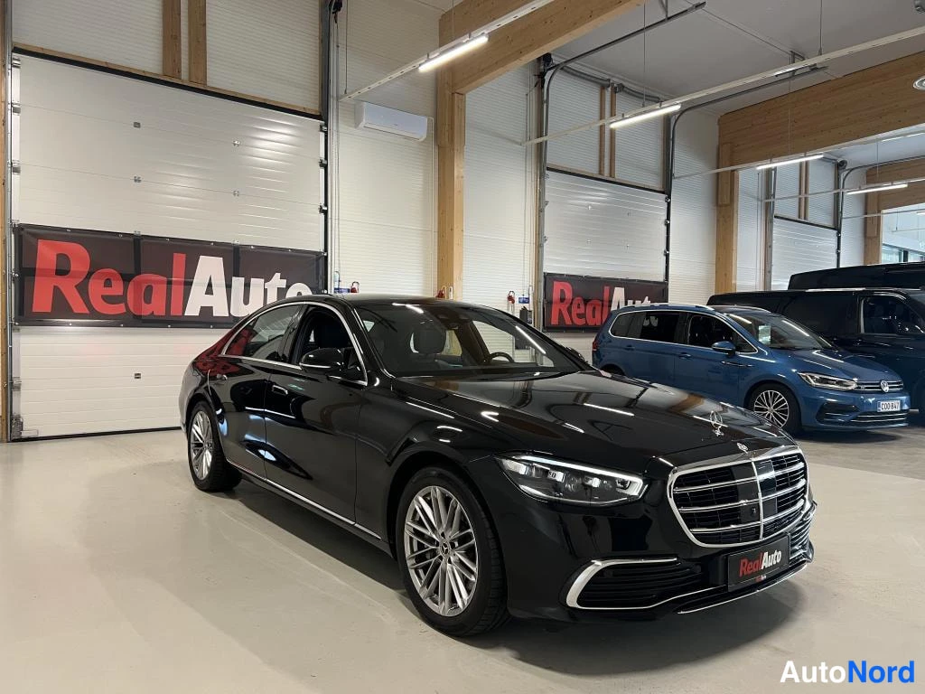 Etuviisto, nokka oikealle: Musta Mercedes-Benz S-luokan sedan etuviistosta oikealta, keula ja sivu näkyvissä hallissa.