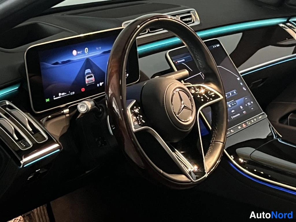 Yksityiskohta: Autojen sisätilakuva: Mercedes-ohjauspyörä, digitaalinen mittaristo ja infotainment-näyttö, tunnelmavalaistus.