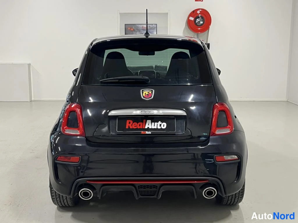 Takaa: Mustan auton takaosa: takavaloja, Abarth-merkki, kaksoispakoputki ja punainen Korkea jännitys -teksti taustalla.