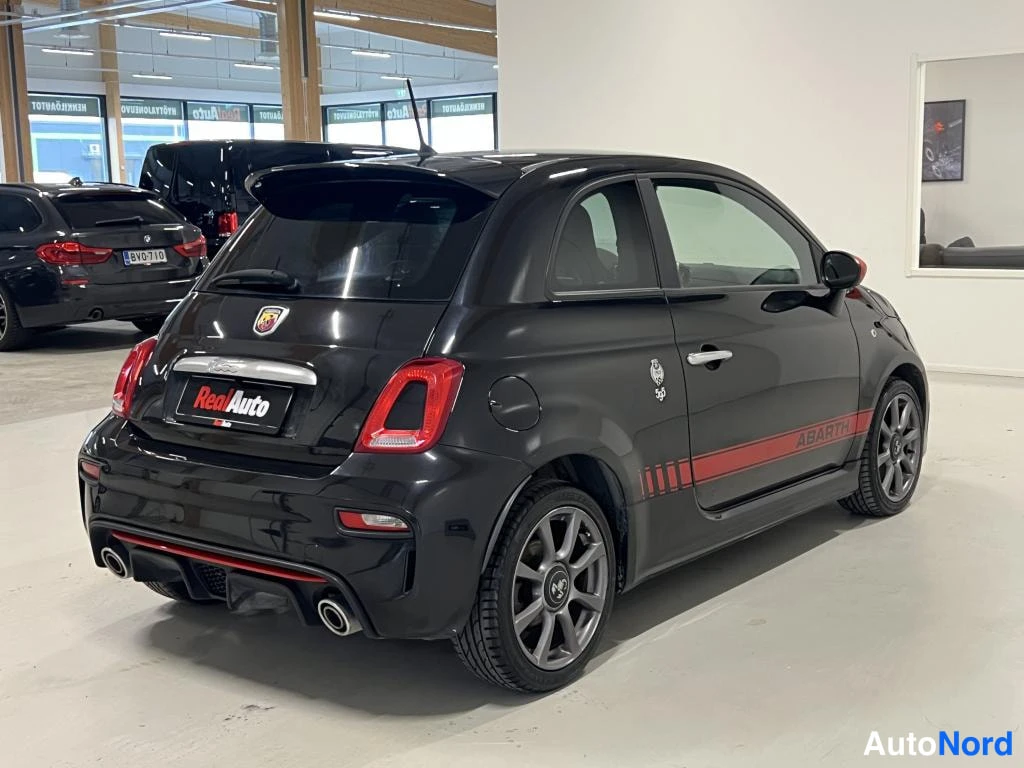 Takaviisto: Mustan auton takakulmanäkymä oikealta: takavalo, Abarth-tunnus, punainen sivukaista ja hopeavanne.