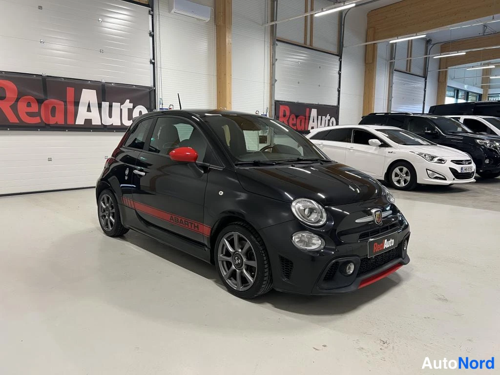 Etuviisto, nokka oikealle: Mustan auton etukulmanäkymä oikealta: pyöreät etuvalot, punainen etusplitteri, Abarth-sivukaista ja Abarth-merkki maskissa.