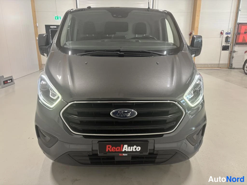 Edestä: Ford Transit Custom -pakettiauto edestäpäin, tummanharmaa, Ford-merkki etusäleikössä.