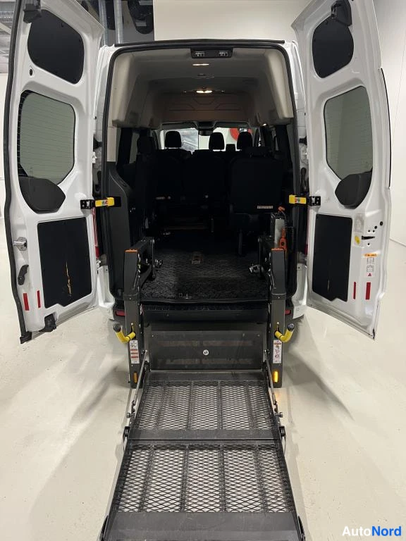 Takaa: Ford Transit Custom -auton takaovet auki ja pyörätuoliramppi laskettuna maahan; rampin molemmin puolin keltaiset kaiteet, sisällä mustat penkit.