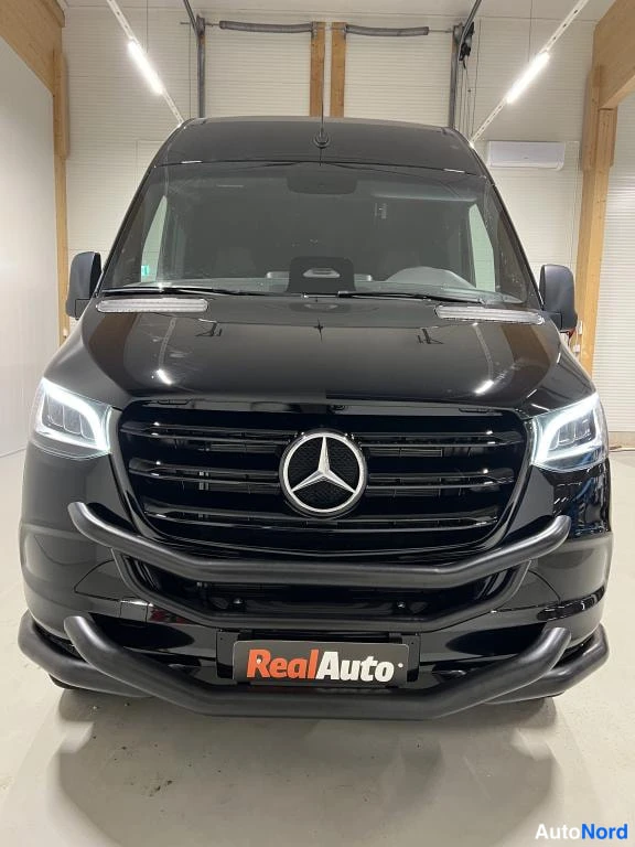 Edestä: Musta Mercedes-Benz Sprinter suoraan edestä, Mercedes-tähti etusäleikössä.