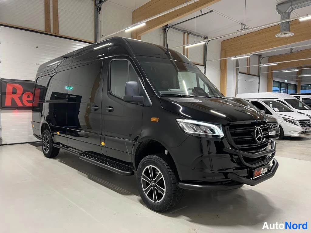 Etuviisto, nokka oikealle: Musta Mercedes-Benz Sprinter -pakettiauto etukulmasta oikealta, kylkijalka ja keulavisiiri näkyvät.