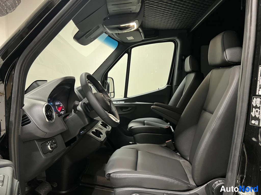 Muu: Kuva kuormatilan takaa: Mercedes-Benz Sprinter -auto sisältä, edessä ohjauspyörä ja instrumentit, takana kaksi mustaa istuinta