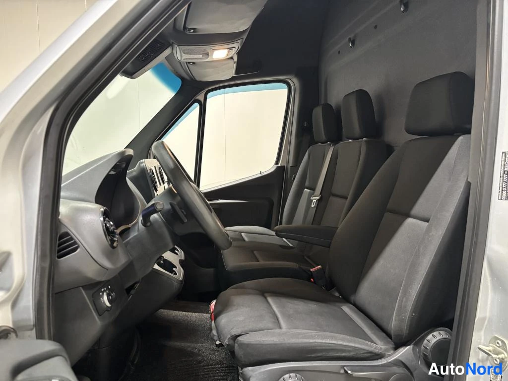 Etuviisto, nokka vasemmalle: Mercedes-Benz Sprinter -pakettiauton ohjaamo edestä vasemmalta kuvattuna, mittaristo, ohjauspyörä, kojelauta ja tuulilasi.