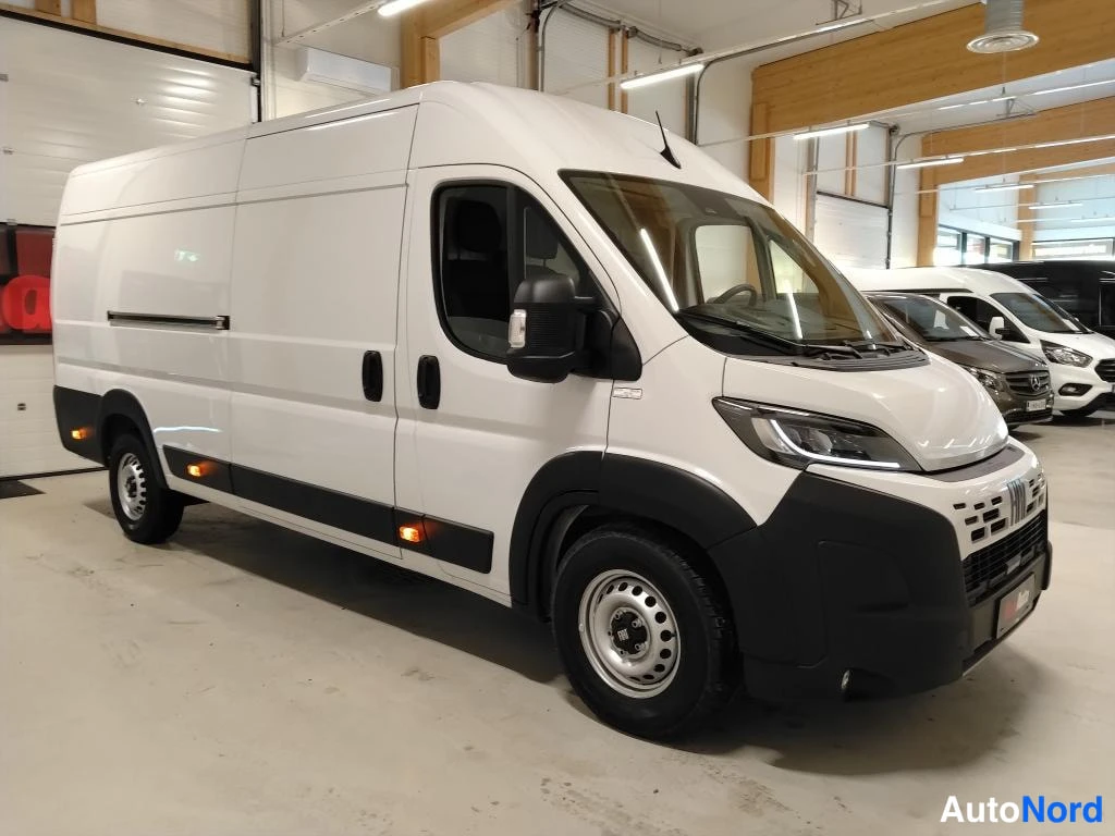 Etuviisto, nokka oikealle: Fiat Ducato -pakettiauto kylki ja keula näkyvät, nokka osoittaa oikealle hallissa.