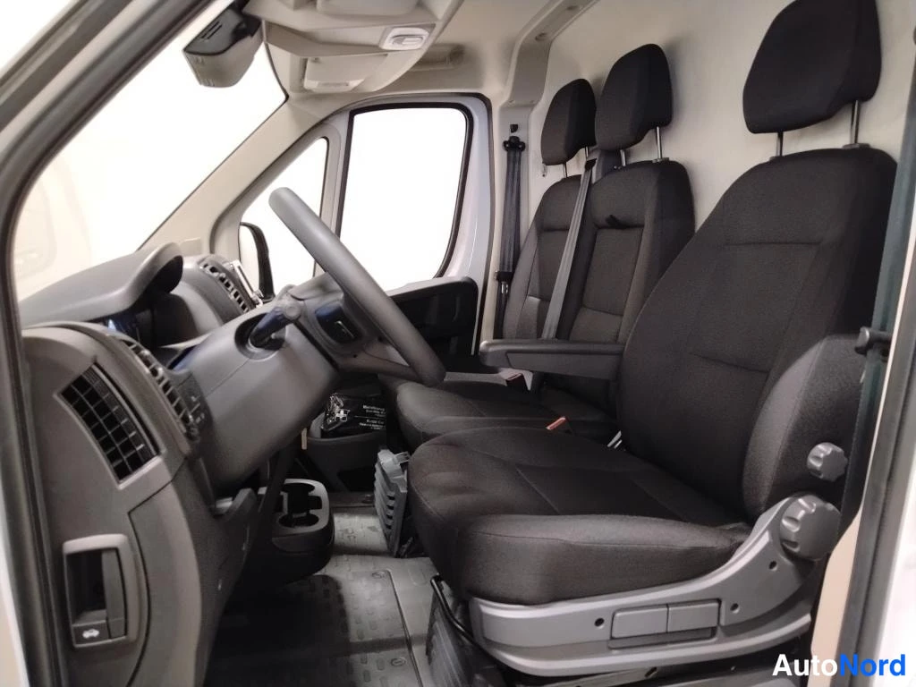 Edestä: Fiat Ducato -pakettiauton ohjaamosta; tummanharmaat kankaverhoillut etupenkit, ohjauspyörä ja kojelaudan osia.