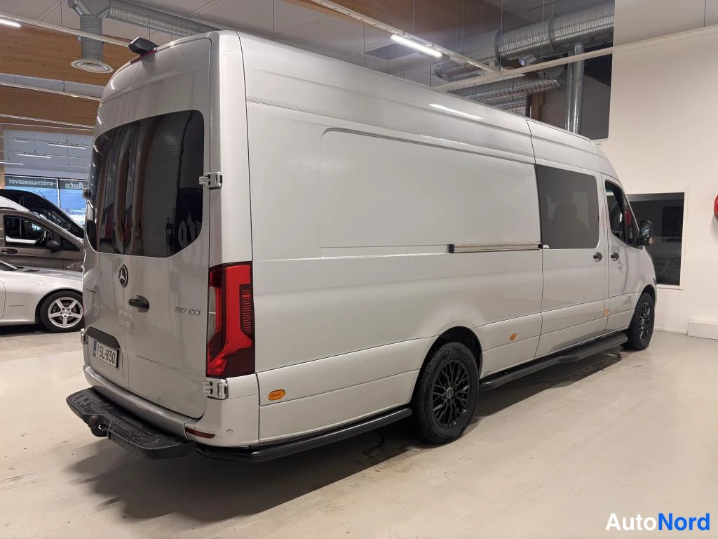 Takaviisto: Hopeaharmaa Mercedes-Benz Sprinter -pakettiauto takaviistosta vasemmalta kuvattuna autotallissa; mustat vanteet ja vetokoukku näkyvät.