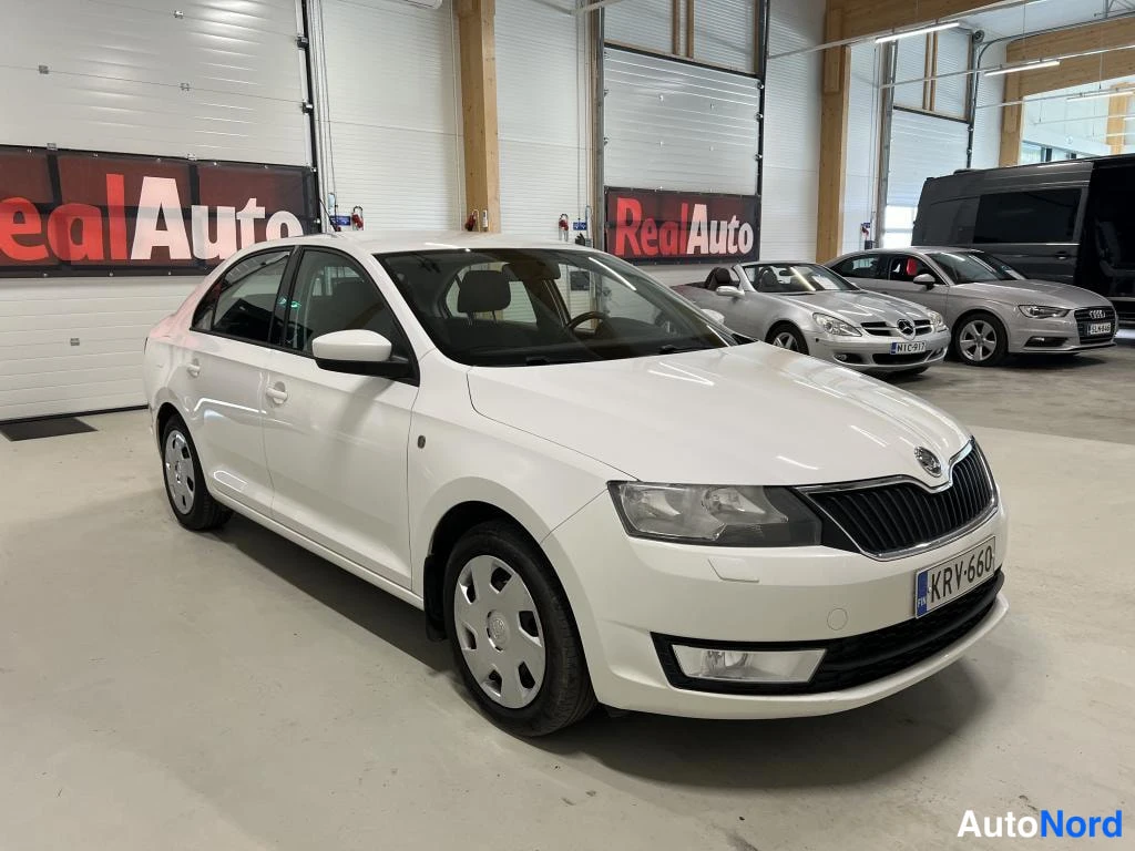 Etuviisto, nokka oikealle: Valkoisen Skoda Rapid -sedan etukulmanäkyvää sisätiloissa, rekisteritunnus, etusäleikkö ja ohjaamo näkyvät.