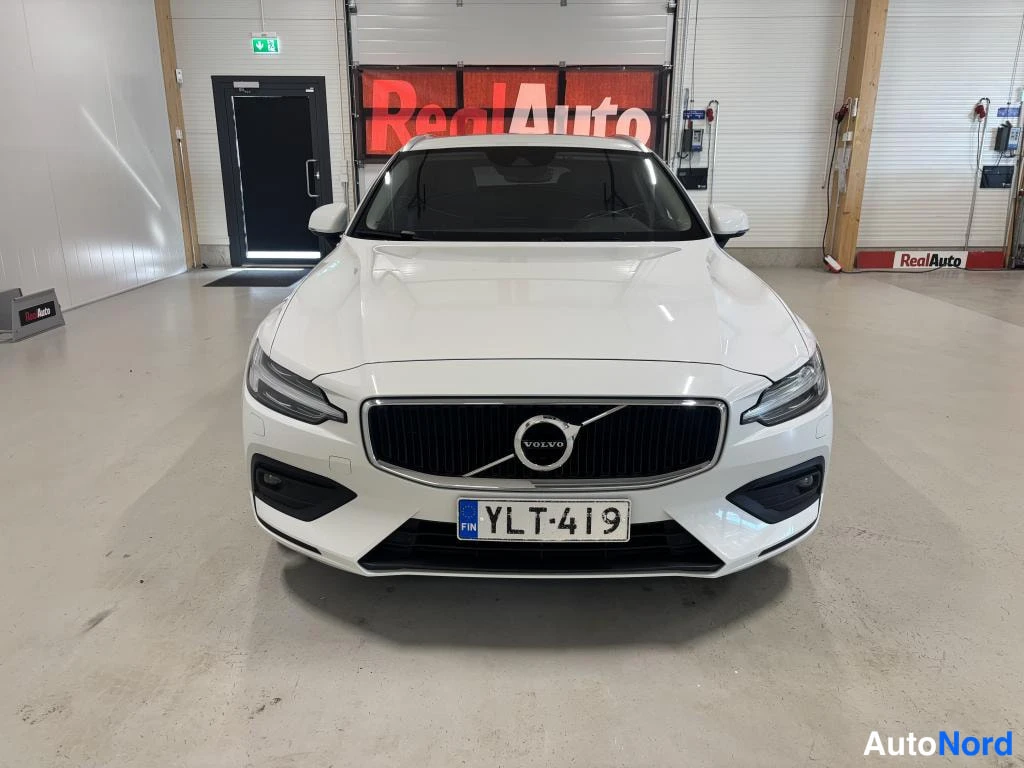 Edestä: Valkoisen farmariauton etunäkymä, etusäleikkö ja Volvo-embleemi, rekisterikilpi.
