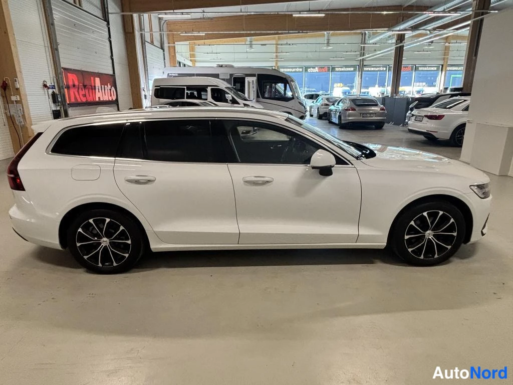 Etuviisto, nokka oikealle: Valkoinen farmariauto sivulta, keula oikealla, autotallissa.