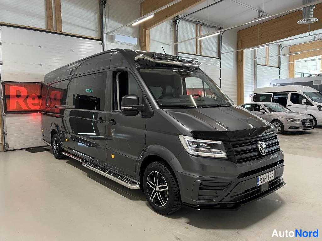 Etuviisto, nokka oikealle: Tummanharmaan Volkswagen Crafter -pakettiauton etunurkkakuva oikealta, joka näyttää keulaa, kylkeä, replayhyitä ja kattotelinevalaisimia.