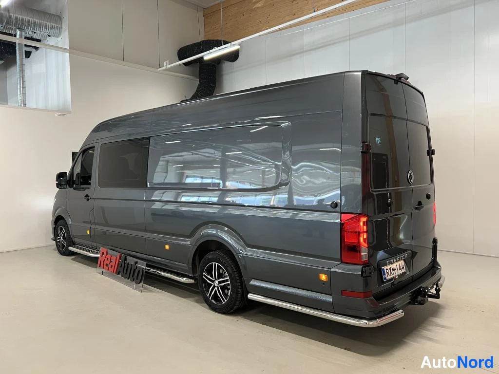 Takaviisto: Tummanharmaan pakettiauton takaosa ja vasen kylki sisätiloissa; rekvisiitissa RealAuto-kyltti.