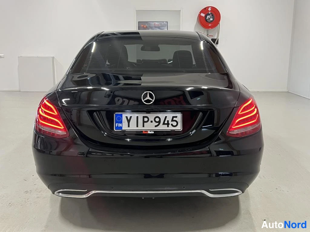 Takaa: Mustan sedanin takanäkymä: Mercedes-tähti puskurissa, punaiset takavalot ja rekisterikilpi.