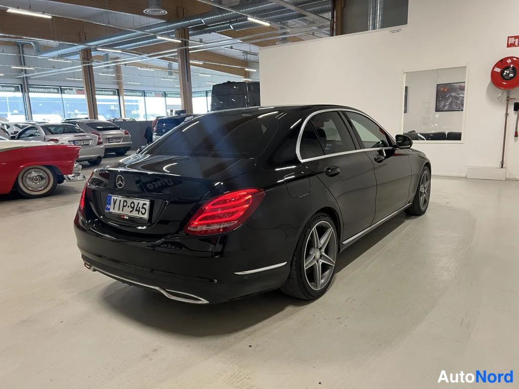 Takaviisto: Musta Mercedes-sedan takaviistosta sisähallissa, rekisterikilpi, viisakkomalliset kevytmetallivanteet.