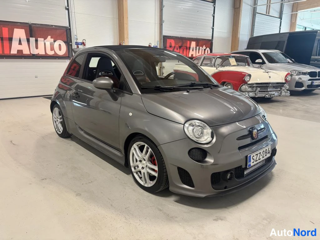 Etuviisto, nokka oikealle: Harmaa Fiat 500 Abarth etukulmasta oikealta, etupuoli ja oikea kylki näkyvillä, kevytmetallivanteet ja punaiset jarrusatulat.