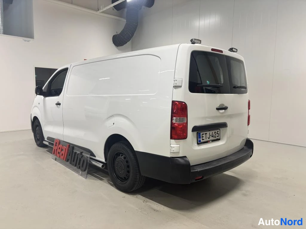 Takaviisto: Valkoinen pakettiauto takaviistosta, rekisterikilpi.