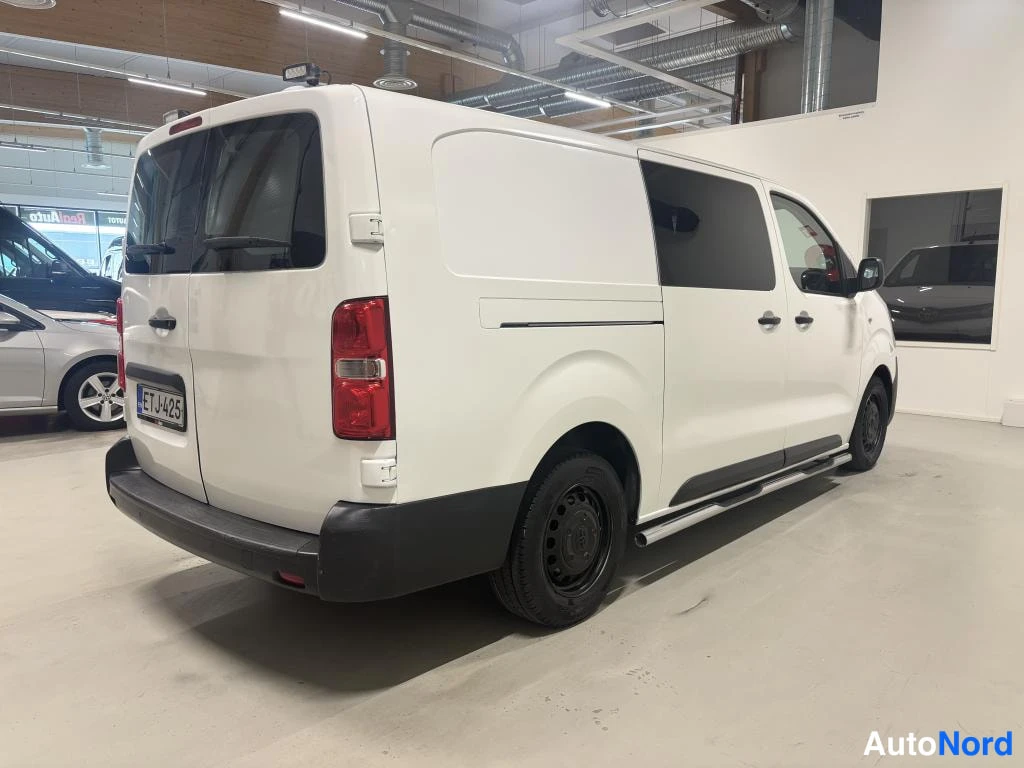 Takaviisto: Valkoinen pakettiauto takaviistosta hallitilassa, rekisterikilpi.