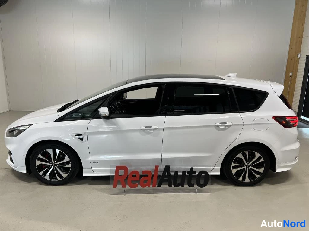 Etuviisto, nokka vasemmalle: Valkoisen Ford S-MAX:n vasen sivu kuvattuna sisätilassa, tumma lasikatto ja tummat vanteet.
