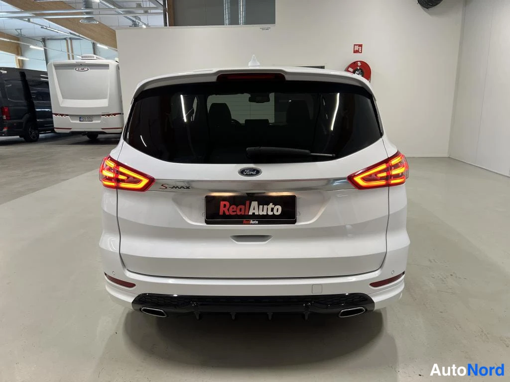Takaa: Valkoisen Ford S-MAX:n takaosa suoraan takaa, 'S-MAX'-teksti ja Ford-merkki takaluukussa, kaksoset pakoputket alhaalla.