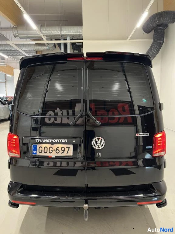 Takaa: Mustan pakettiauton takaosa suoraan takaa, peräovessa TRANSPORTER- ja 4MOTION-tekstit, rekisteritunnus ja vetokoukun pallo.