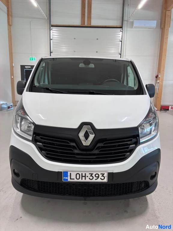 Edestä: Renault Trafic -pakettiauton etupää näkyvissä: valkoinen kylki, mustat puskurit ja etusäleikkö, Renault-tunnus keskellä, rekisterikilpi L0H-393.